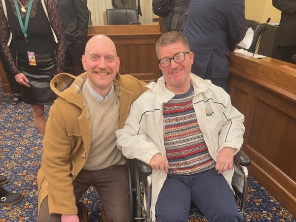 Two men pose for a photo inside a conference room.