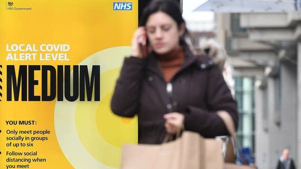 A shopper talks on her mobile phone as she walks past a sign displaying the Local COVID Alert Level as "Medium", on a bus-stop along Victoria Street, central London on October 15, 2020, as Londoners face more stringent novel coronavirus COVID-19 restrictions as the number of cases rises.