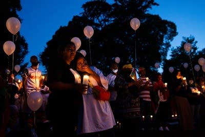 Two women lean on each other while holding candles.