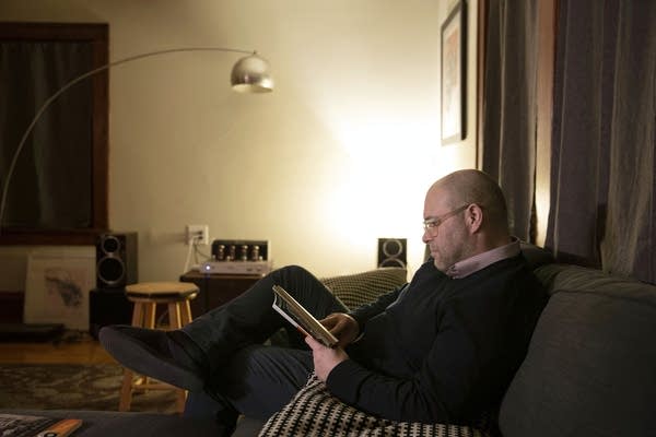 A man sitting on a gray couch reads a book.