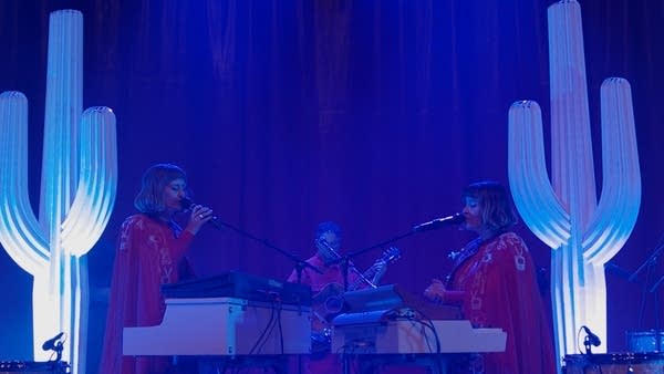 Three musicians stand and perform between two giant stagecraft cacti 