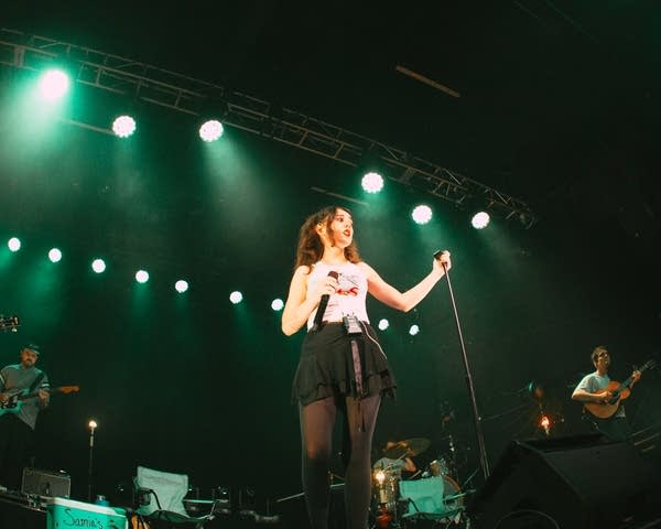 A woman sings into a microphone on a lighted stage.