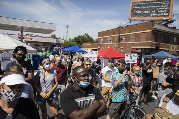 A crowd of people stand in a street. 