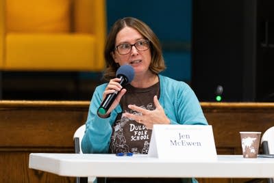 A woman holds a microphone and speaks to a crowd.