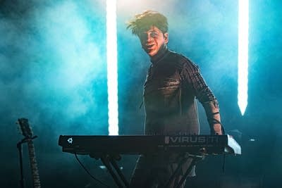 A man standing by a synthesizer onstage smiles during a concert