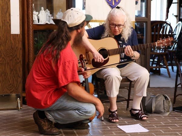 a man crouches next to a woman playing a guitar