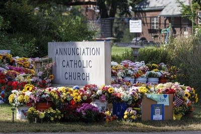A large number of flower bouquets are placed around a stone sign for Annunciation Catholic Church.