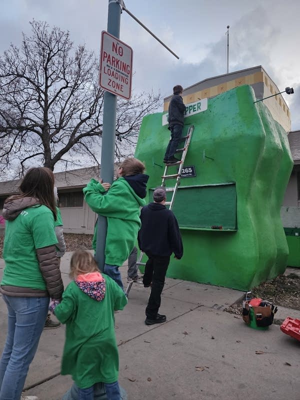 People stand next to a green pepper
