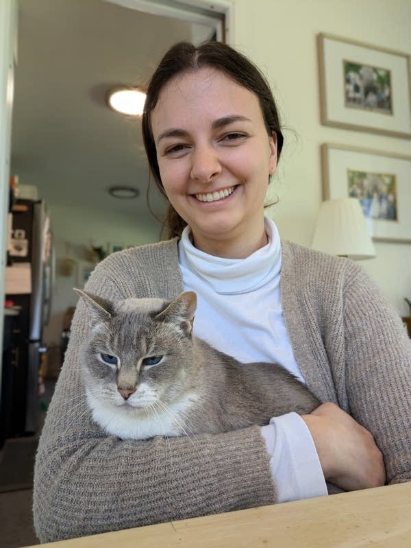 A woman poses for a photo while holding her gray and white cat.