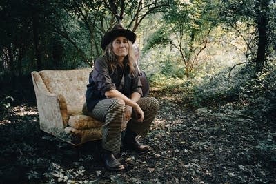 A woman sits on an upholstered chair in the middle of the woods