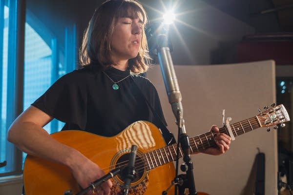 A woman sings and plays guitar in a recording studio