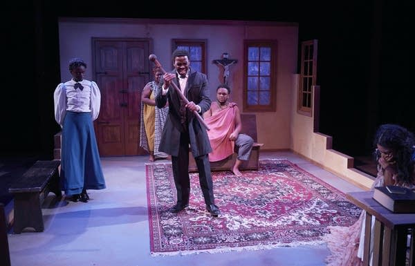 On a theater stage, four people of African descent stand in a living room 