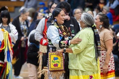 Two women embrace in the middle of a crowded gymnasium.