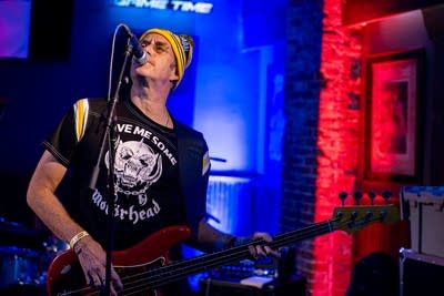 A man sings and plays bass onstage in a music venue