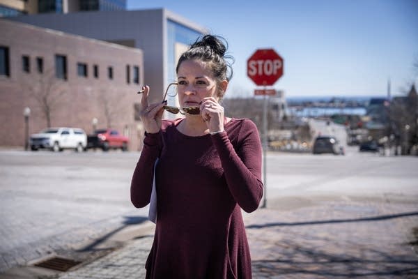 A woman puts on sunglasses while standing on a street.