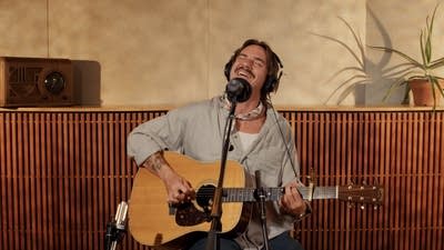 A musician sings and plays guitar in a recording studio
