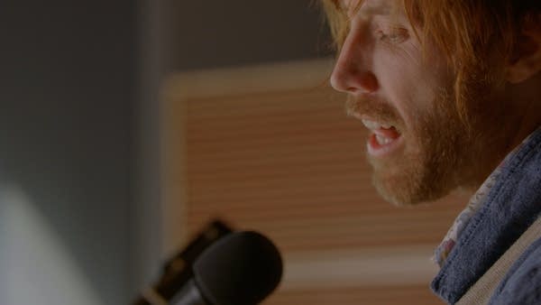 A man sings and plays guitar in a recording studio