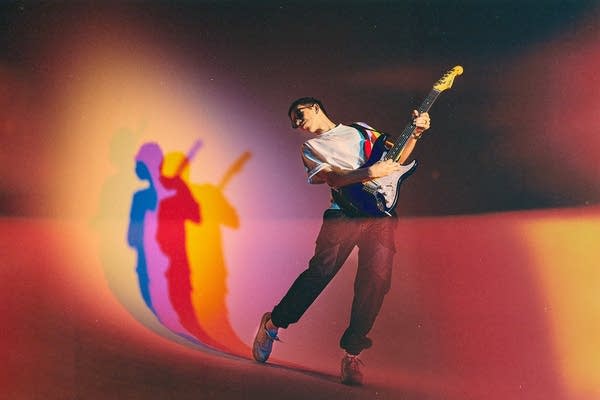 A man in sunglasses plays guitar while posing for a studio portrait