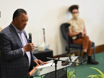 Jesse Jackson holds a microphone and stands behind a podium.
