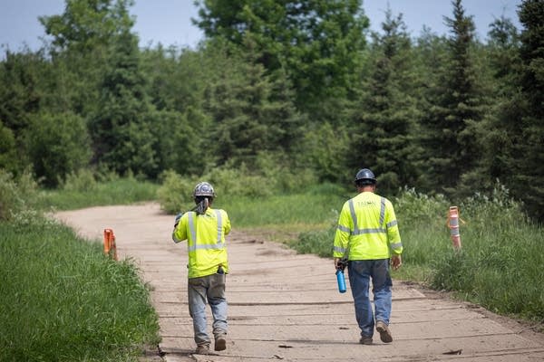 Two people wearing hi-vis and hardhats walk on a path
