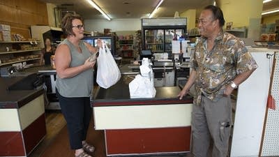 A woman picks up a plastic grocery bag as she talks with a man in a store.