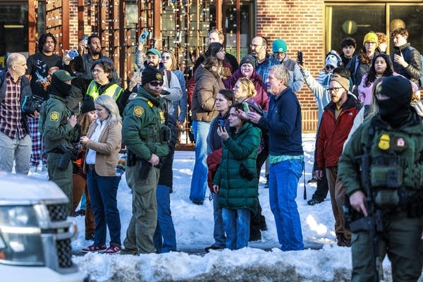 A crowd of onlookers outside a school record ICE agents with their phones.