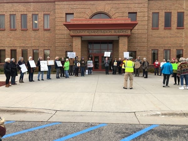 A group of people hold signs and line up outside the County Administration Building.
