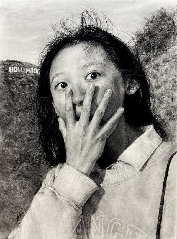 A charcoal drawing of a woman with her hand over her face and the Hollywood sign behind her