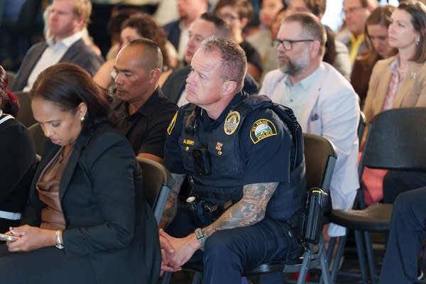 A police officer leans forward in his chair while listening to a speech.