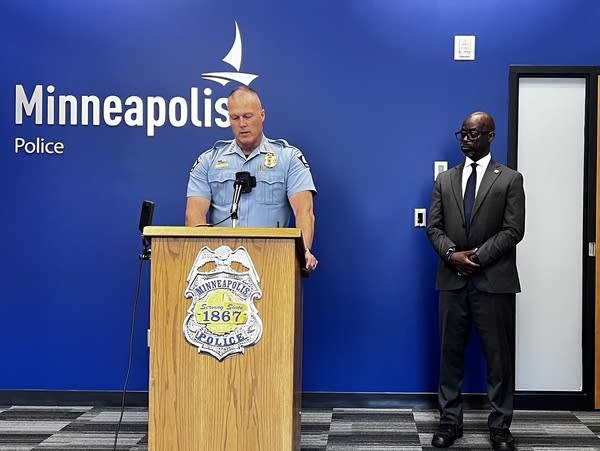 A police officer speaks at a podium while a man in a suit stands next to him.