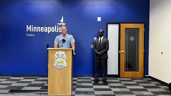 A police officer speaks at a podium while a man in a suit stands next to him.
