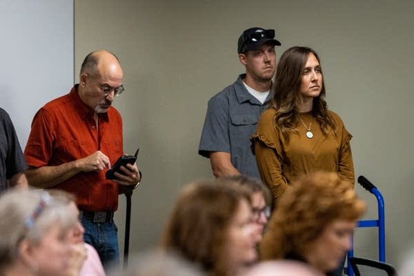 A woman stands and watches people talk