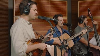 Three musicians sing and play instruments in a recording studio