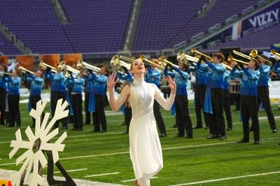 A marching band performs on the field of a football stadium.