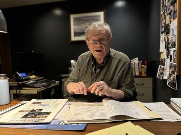 A man sits at a desk covered in papers.