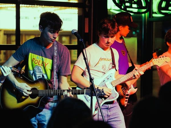 Three young men play guitars on a concert stage.