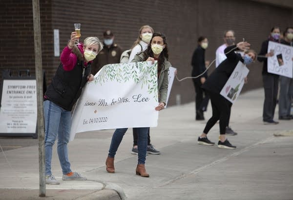 People on a sidewalk wear masks and hold signs