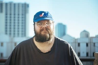 A man in a Montreal Expos baseball cap stands on a rooftop in Tulsa