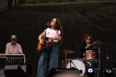 Waxahatchee's Katie Crutchfield sings into a microphone and strums a guitar.
