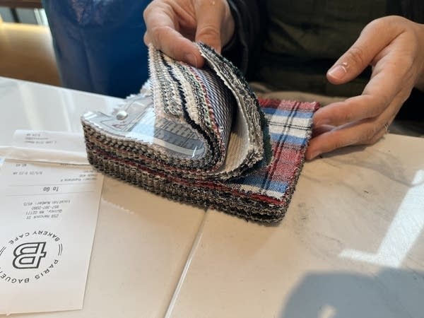 Joanna Lynch flips through a swatch booklet of fabric samples. A red and blue plaid is shown.