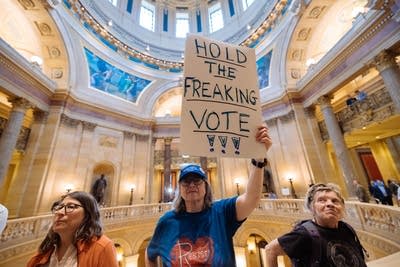 A protester holds a sign reading "HOLD THE FREAKING VOTE!!!"