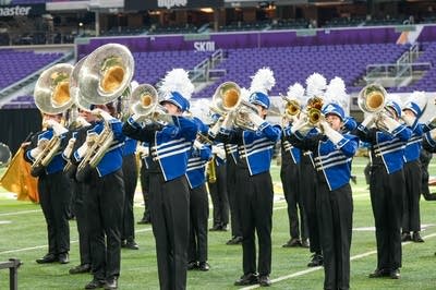 A marching band performs on the field of a football stadium.