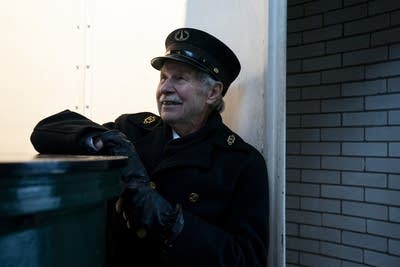 A man dressed as a lighthouse keeper leans on a railing and smiles.