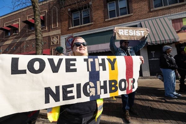 A protester carries a sign reading "Love thy neighbor."