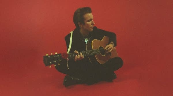 A musician sits on the floor playing guitar