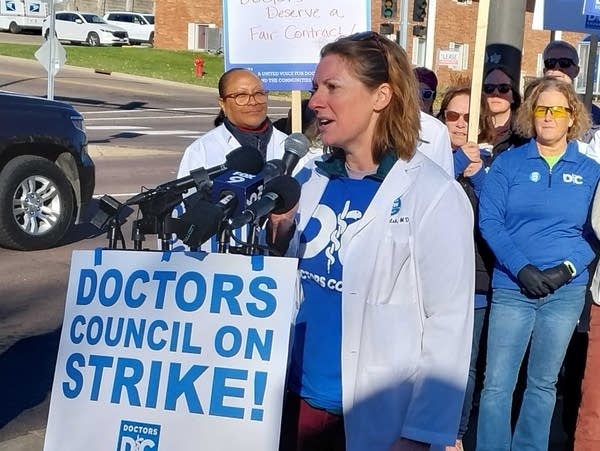 A woman in a lab coat speaks at a podium with microphones