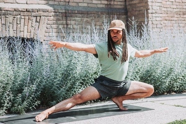 man doing a yoga pose outside wearing t-shirt and shorts with a hat