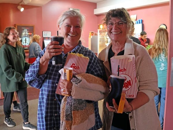 two women smile while holding popcor and soda containers