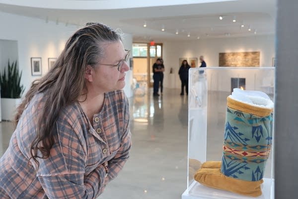 A woman in a museum leans down to look at a pair of boots behind a glass case.