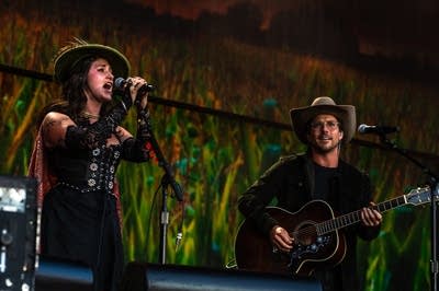 Two people in stylish hats perform on a large outdoor stage